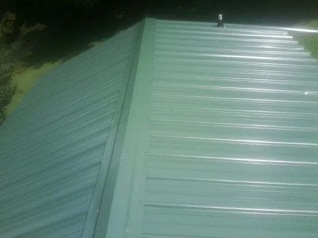 New green metal panels meeting at the ridge of a roof — Flat Roof Repair work by our crew in Warren